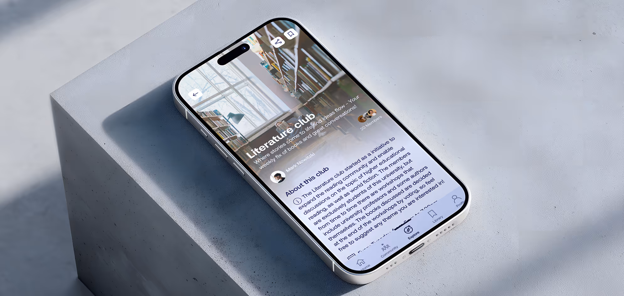 Smartphone lying on a gray block displaying a Literature Club app page with details about the club and navigation icons.